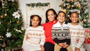Family wearing coordinated holiday sweaters poses together by Christmas decorations.