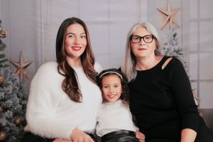 Three people pose together in front of a decorated Christmas tree with star ornaments.