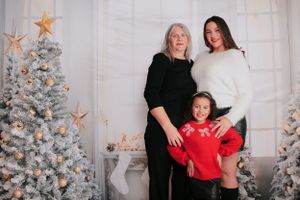 Three generations pose together by decorated Christmas tree with star ornaments.