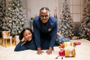 Couple posing playfully on floor with Christmas gifts and decorations.