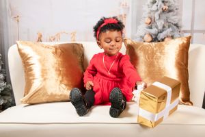 Festive holiday scene with red outfit against gold pillows and Christmas decor.