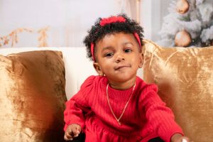 Christmas portrait featuring red sweater and gold accent pillows on white couch.