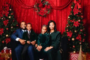 Family holiday photo session with festive red backdrop and decorated Christmas trees.