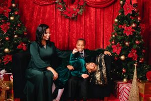 Family group poses on red velvet backdrop with Christmas decorations and trees.