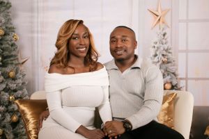 A couple poses for a holiday photo in front of decorated Christmas trees and a gold star ornament.