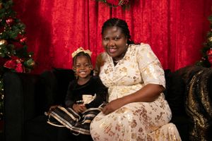 A holiday portrait in front of red curtains and Christmas trees with decorative lighting.
