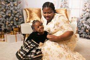 A joyful moment is shared between two people on a gold chair with Christmas trees in the background.