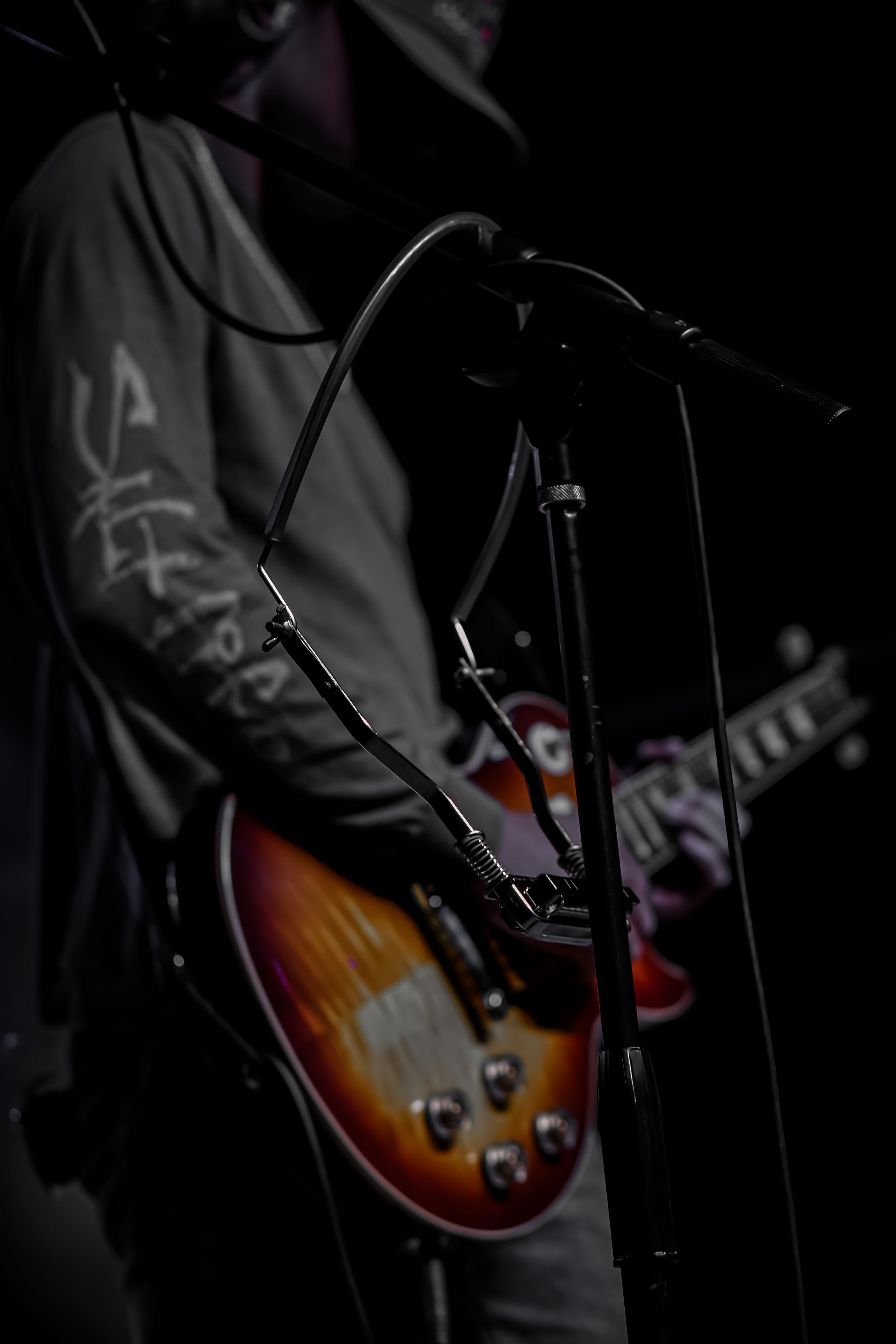 Sunburst electric guitar and microphone stand silhouetted against dark concert stage background.