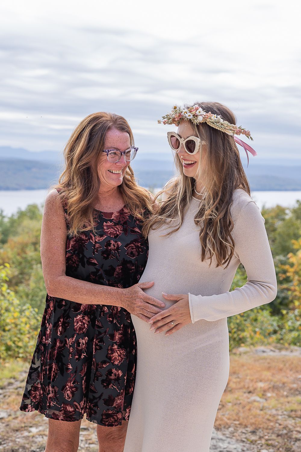 Two women sharing a joyful moment outdoors with one wearing a floral dress and another in a white dress with flower crown.