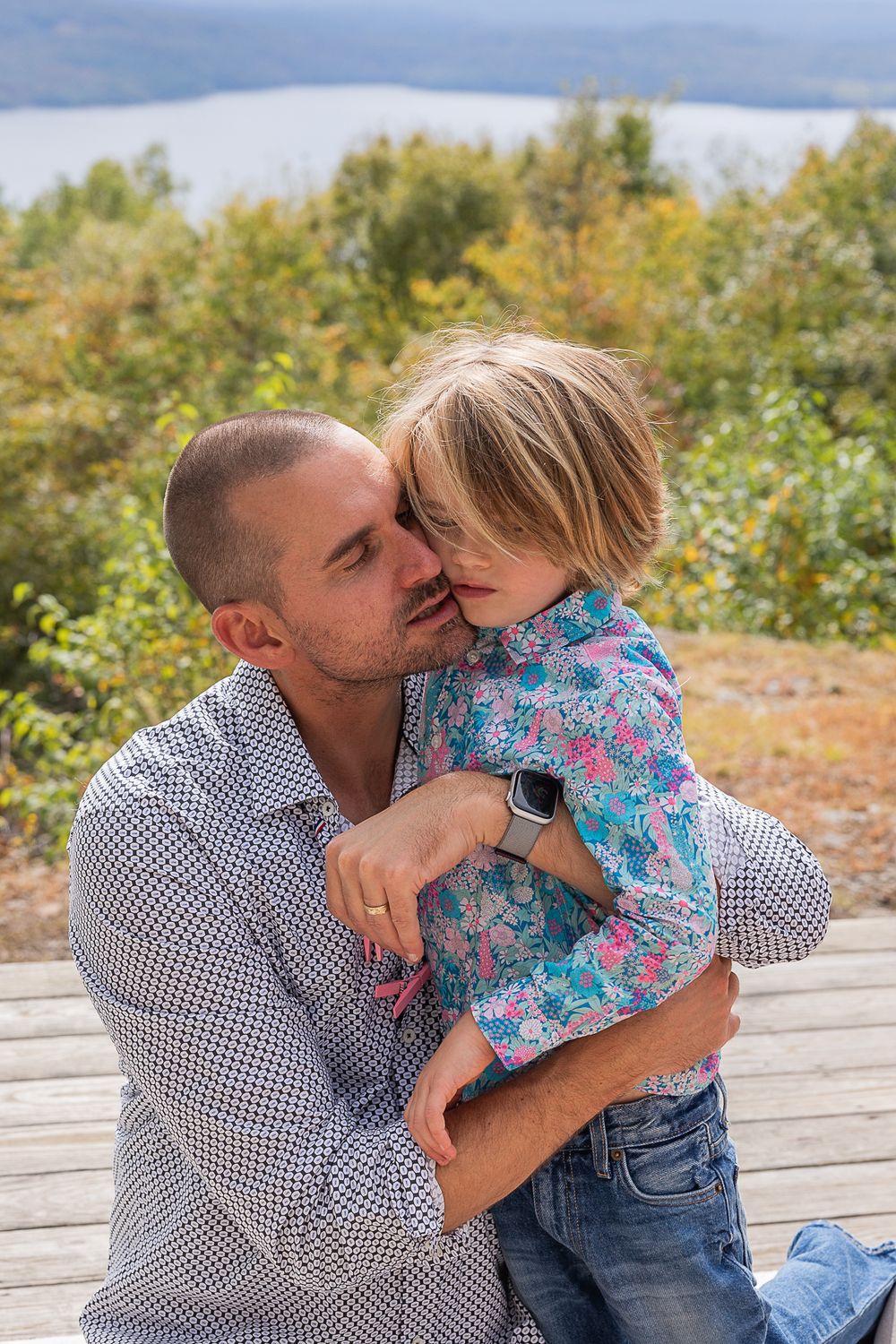 Tender family moment captured on an outdoor deck with scenic mountain views in the background.