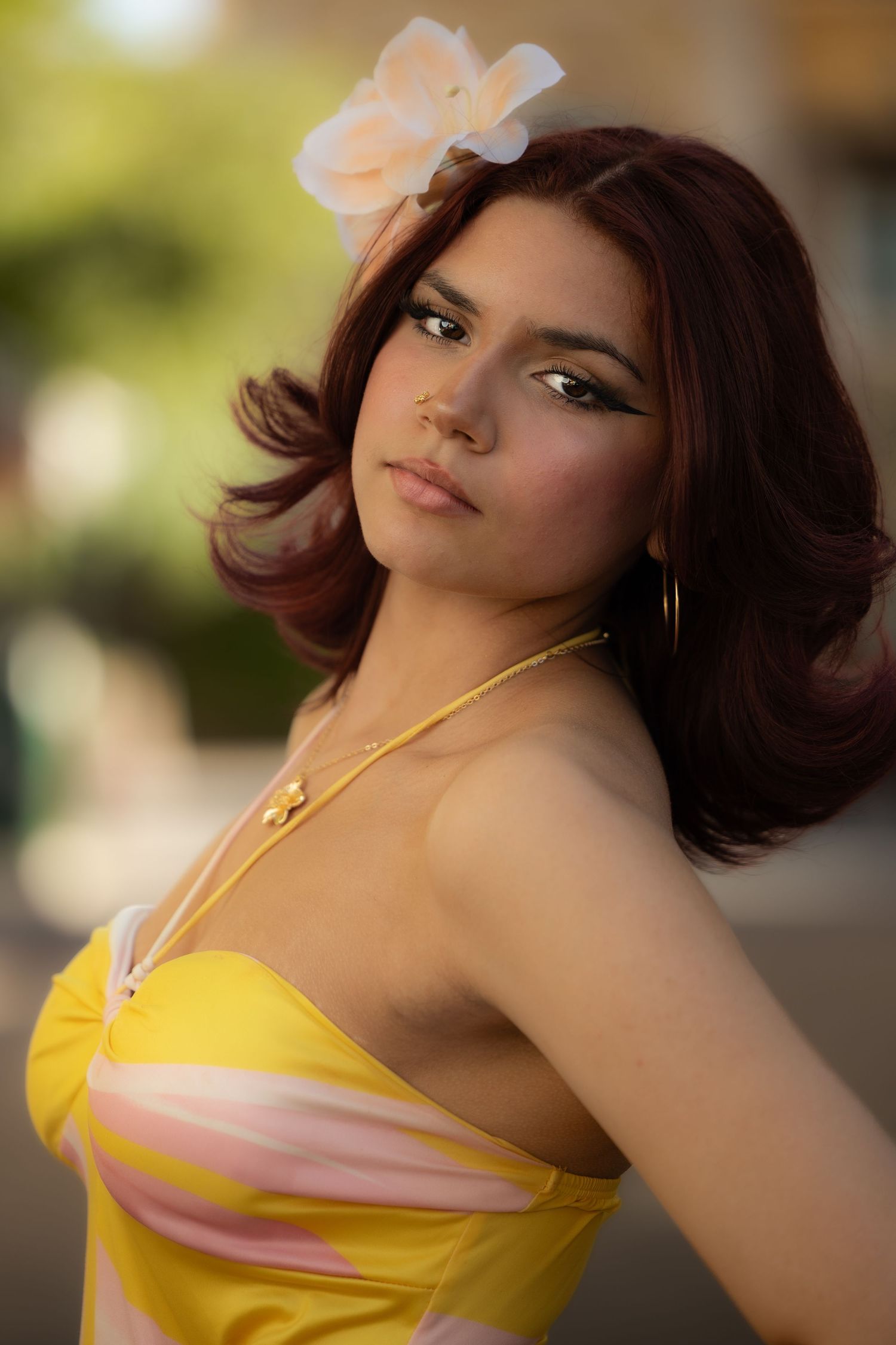 A model poses in a yellow sundress with a peach flower accessory against a soft bokeh background.