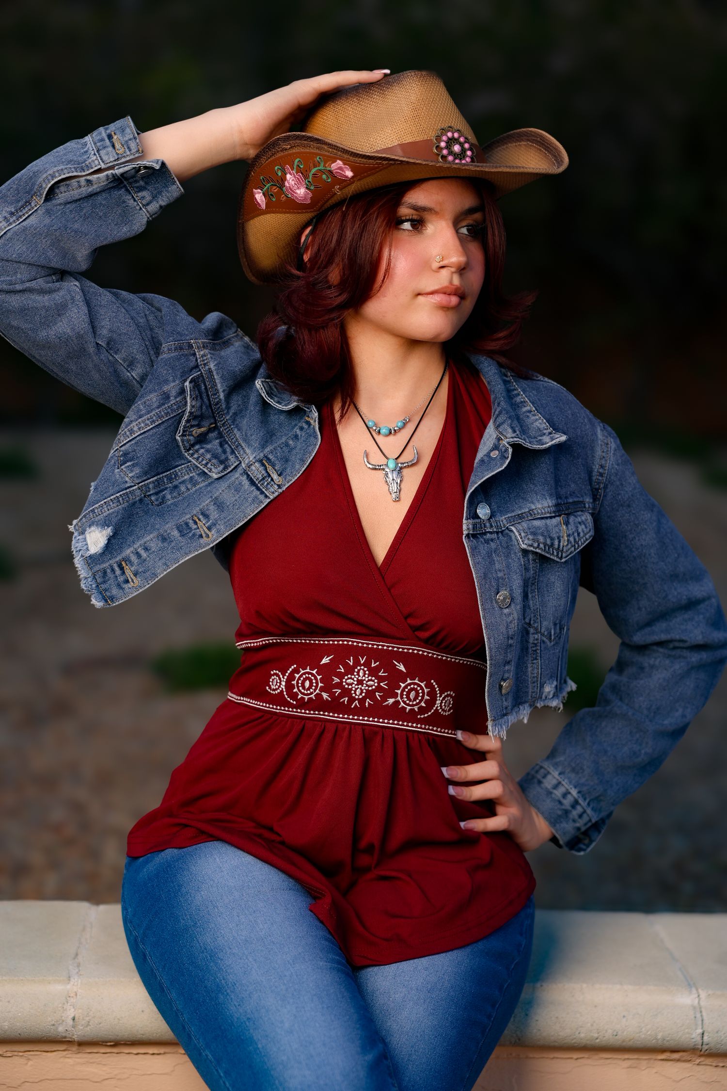 Western style outfit featuring denim jacket, brown leather cowboy hat, red top with embroidered waist belt and blue jeans.
