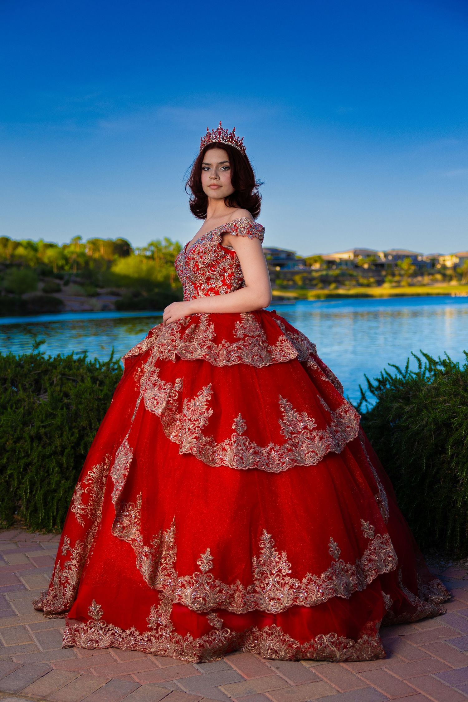 Red ball gown with ornate lace detailing photographed against scenic lakeside backdrop during golden hour.