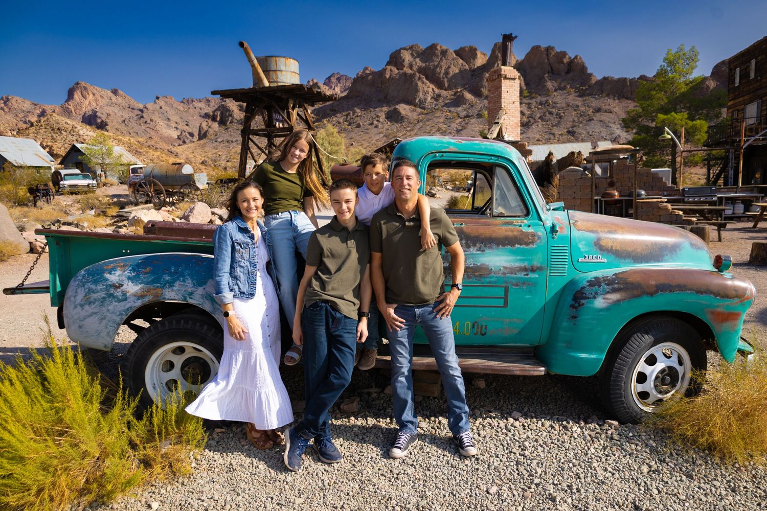 A group poses by a vintage turquoise pickup truck with desert mountains in the background.