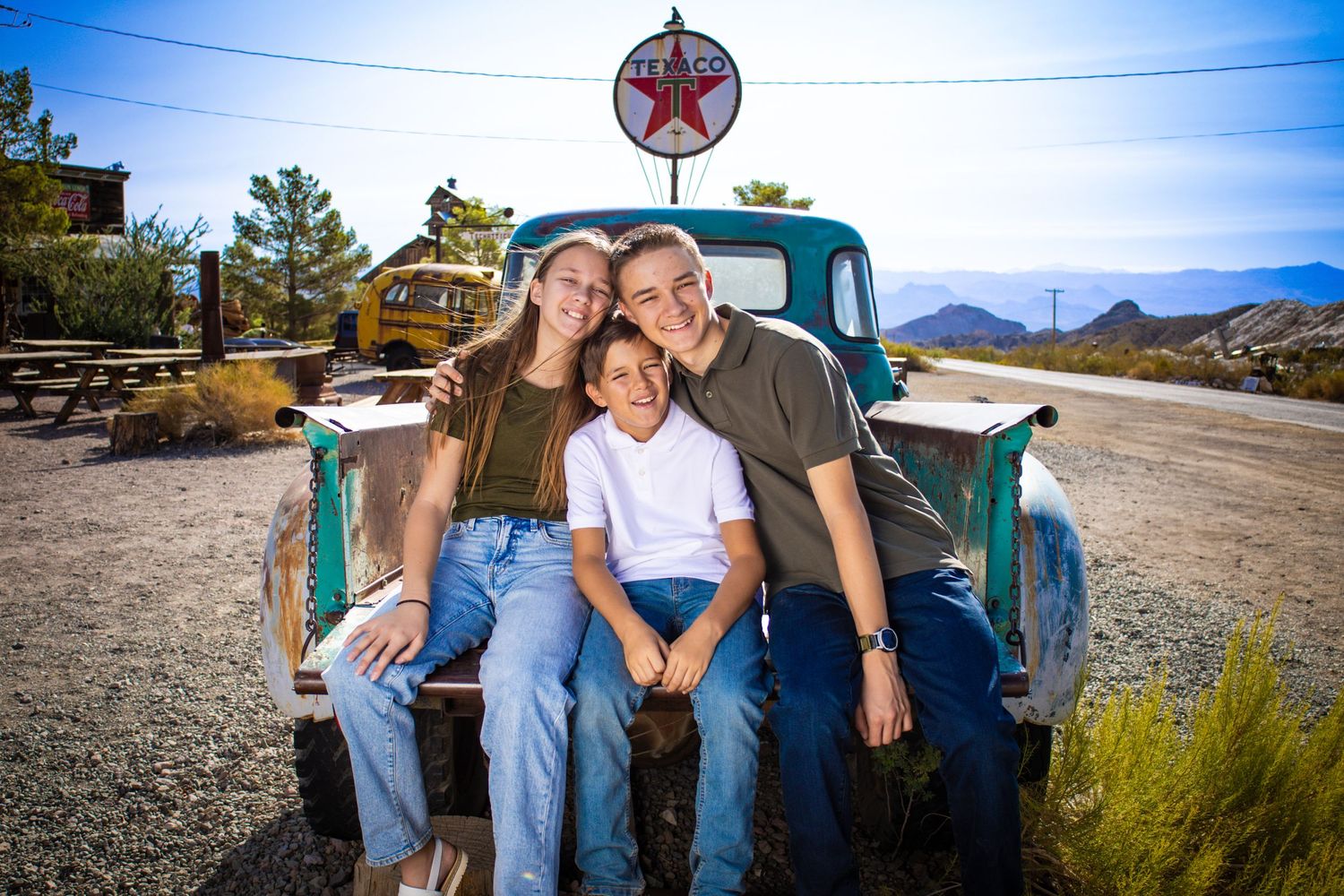 A family group poses on the back of an old turquoise truck with mountains and sky in the background.