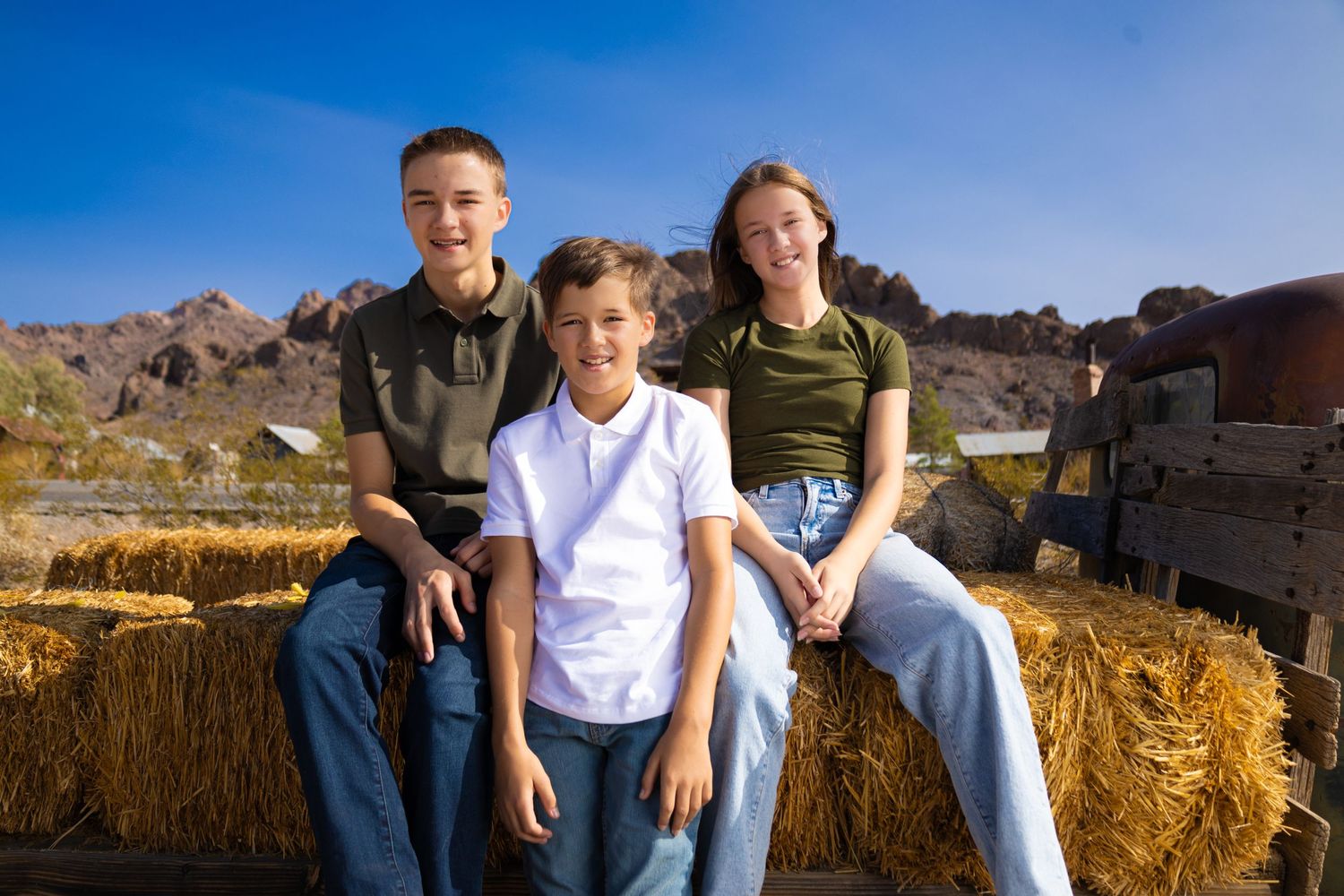 Three people sit on hay bales with desert mountains visible in the background.