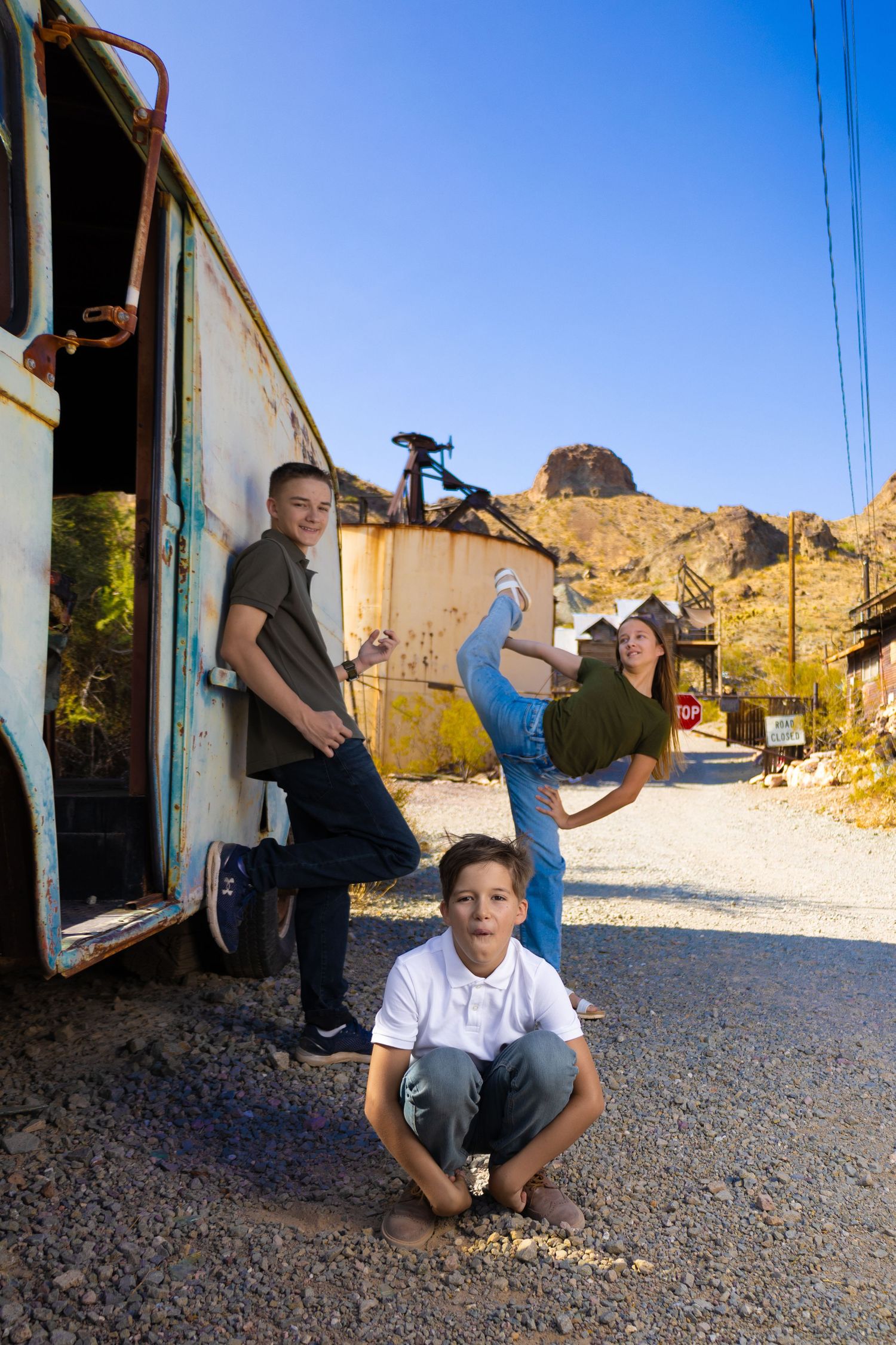 Young people pose playfully around an old van in a desert landscape with rocky mountains.