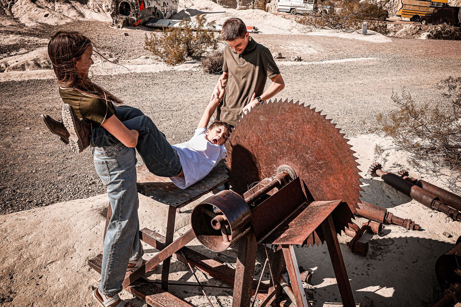 Two people examine a large rusty circular saw blade in an outdoor desert setting.