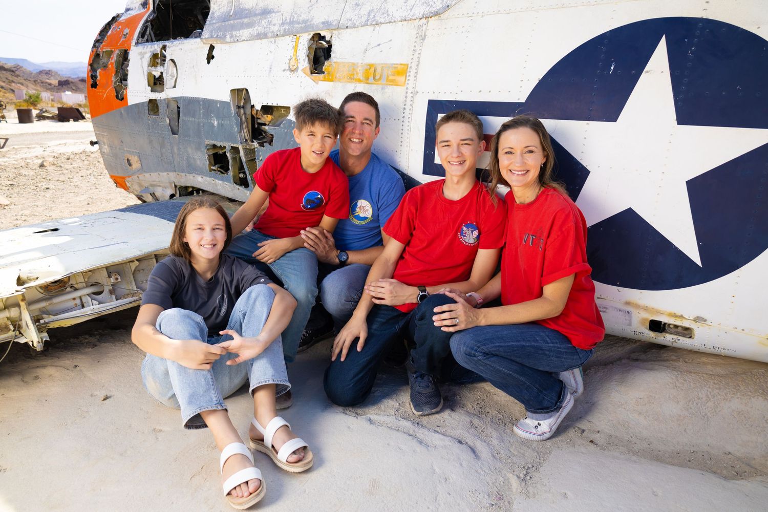 A group in red shirts sits together against a vintage military aircraft with a star emblem.