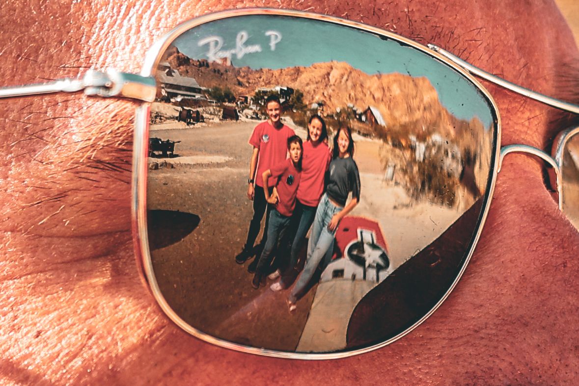 Reflection of people in red shirts against desert mountains captured in sunglasses lens.