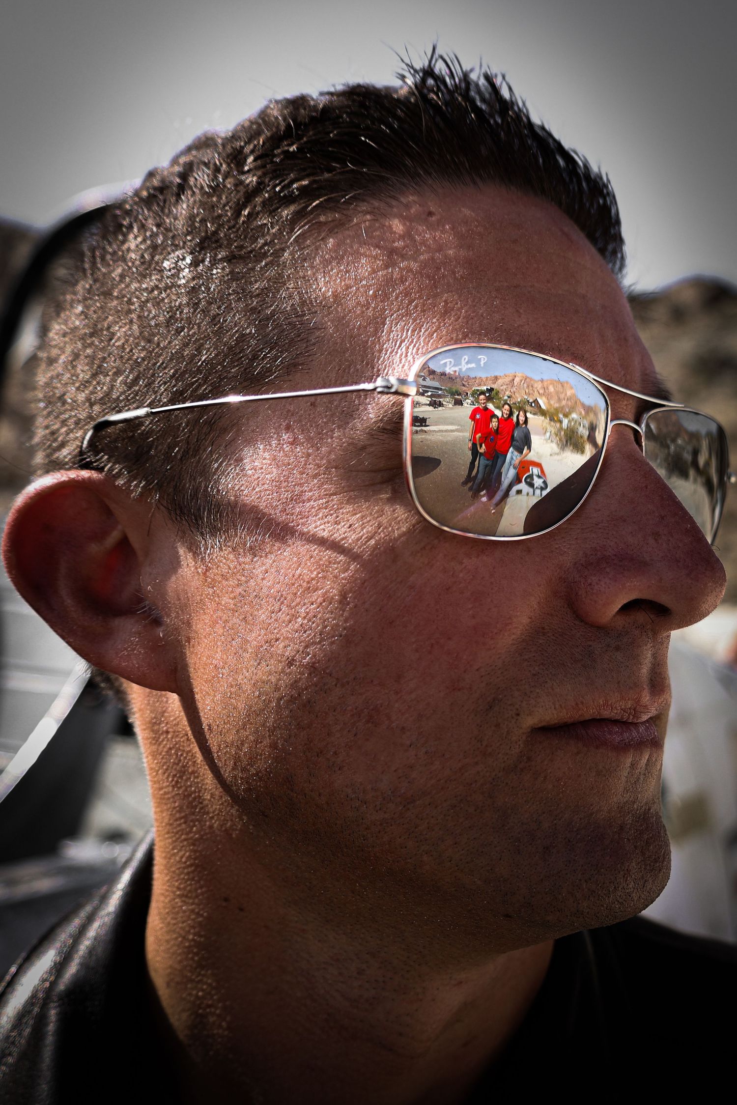 Close-up of sunglasses showing reflection of desert landscape and figures in red.