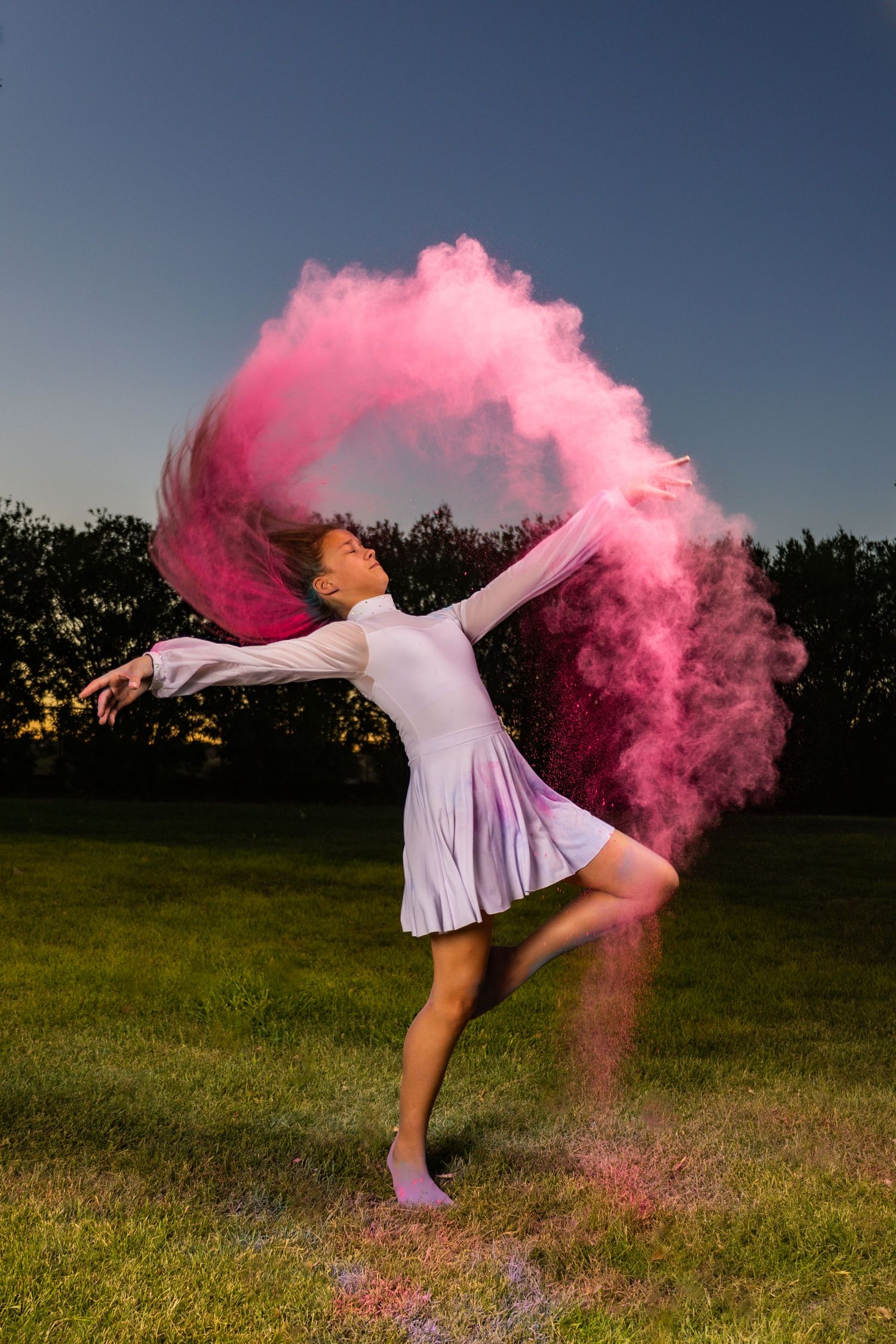Dancer in white dress creates dramatic pink powder effect during outdoor performance.