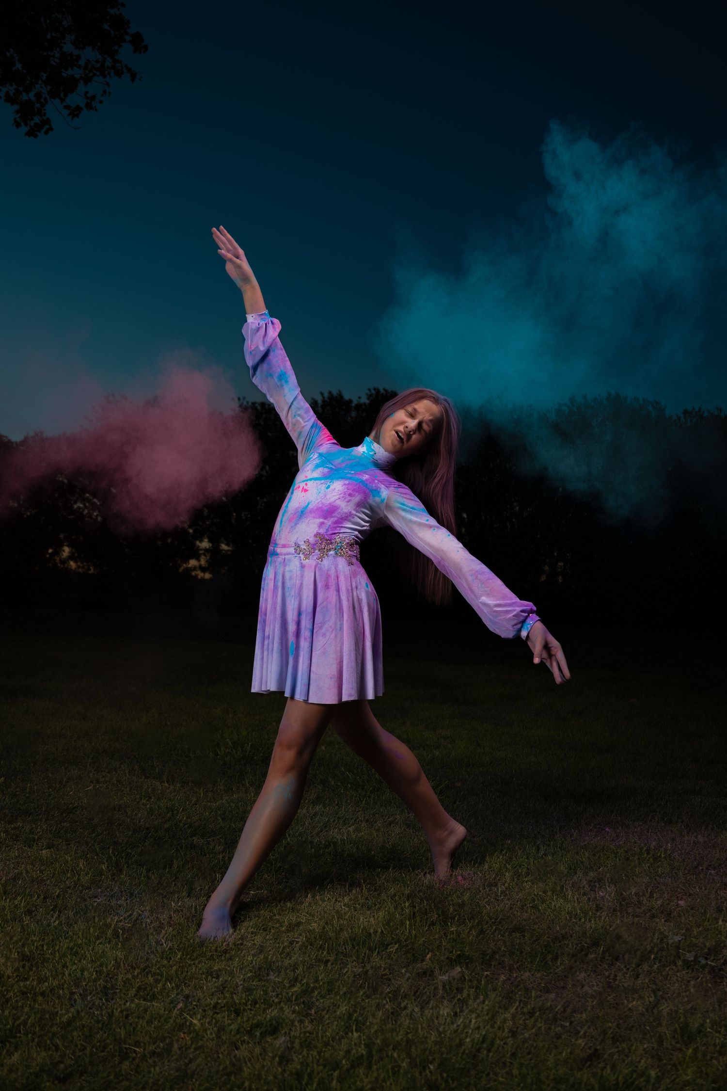 Artistic dance pose with colorful powder effects against night sky.