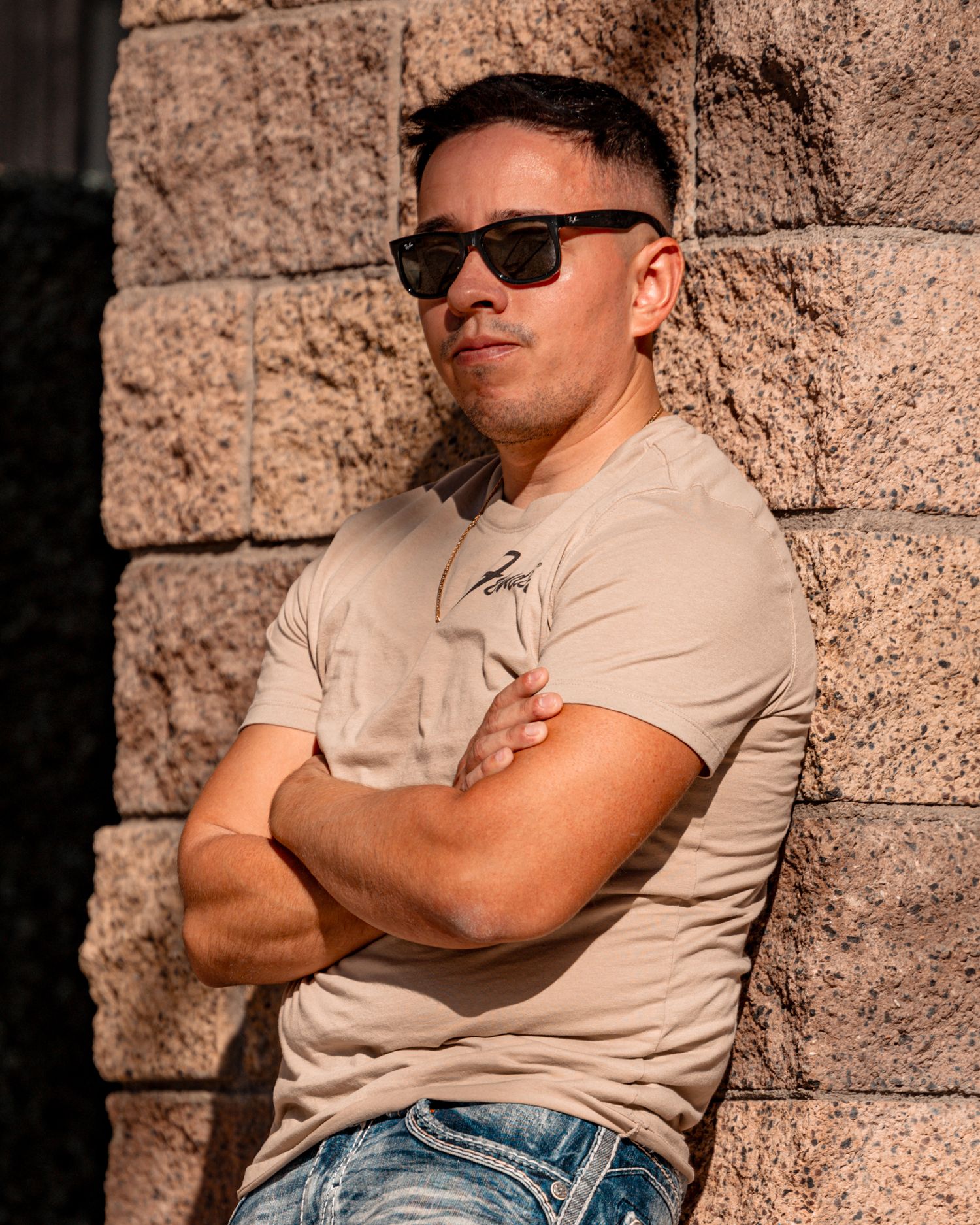 Person in beige shirt and sunglasses poses against textured stone wall.