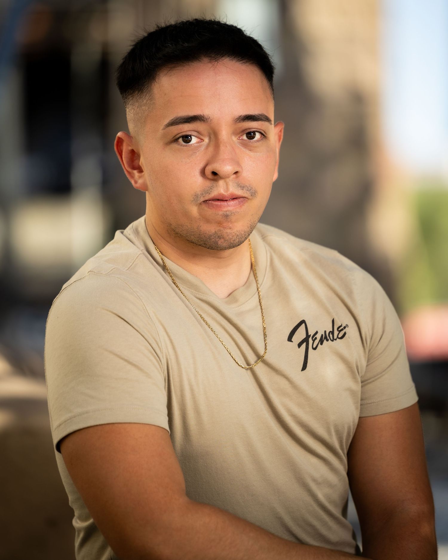 Portrait of a person wearing a beige t-shirt with text in an outdoor setting.