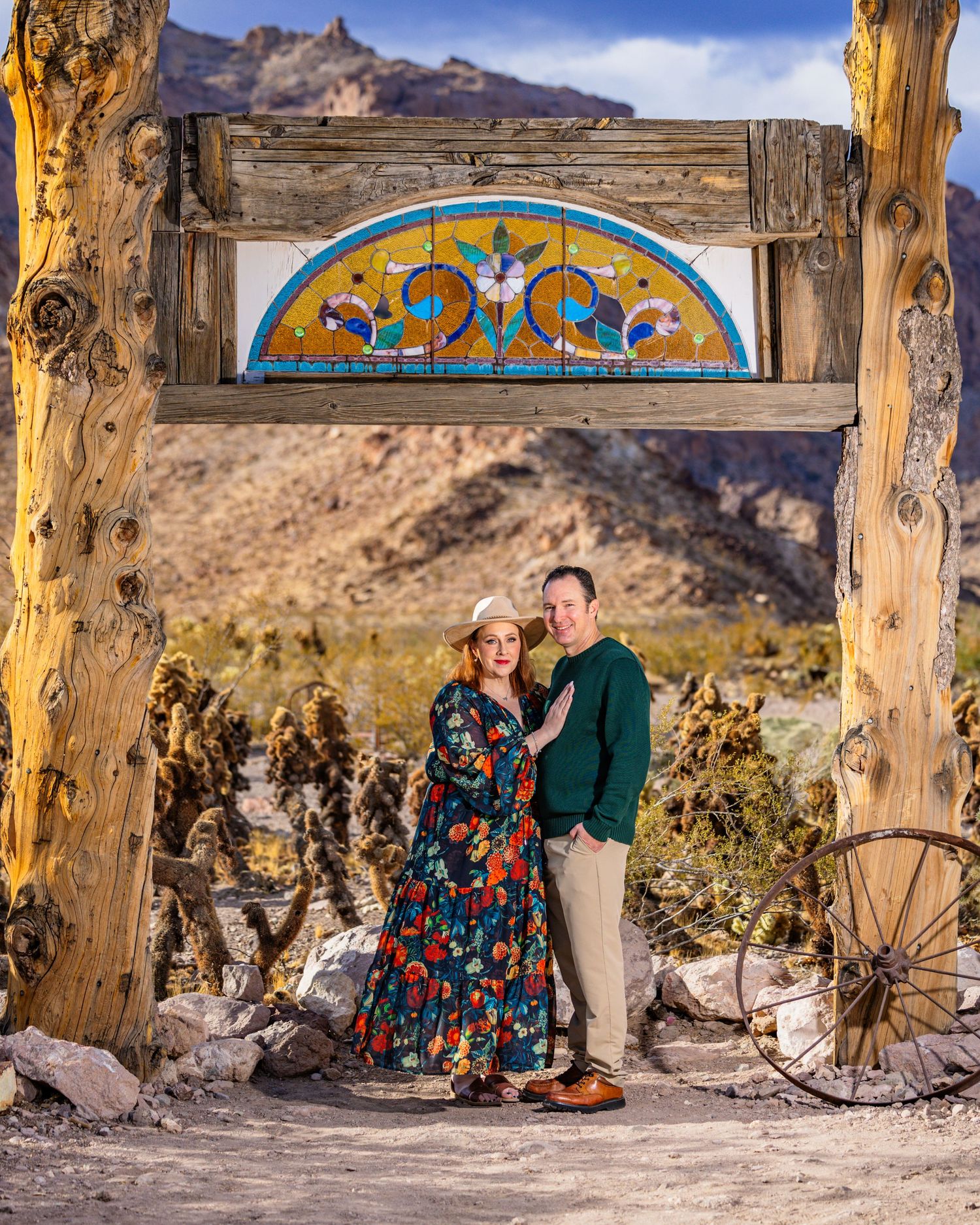 Couple poses under decorative archway with desert mountains in background.