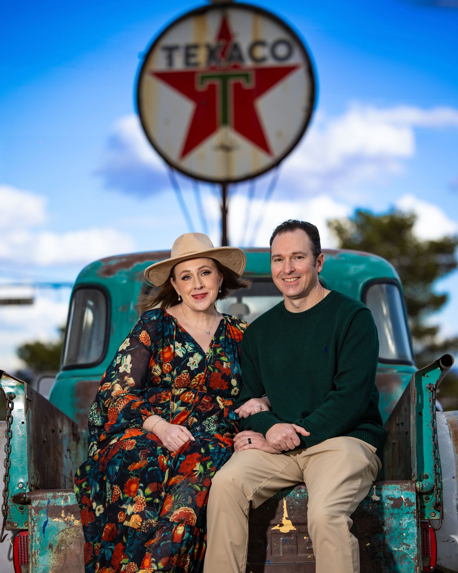 Couple poses in front of vintage truck with iconic Texaco sign in background.