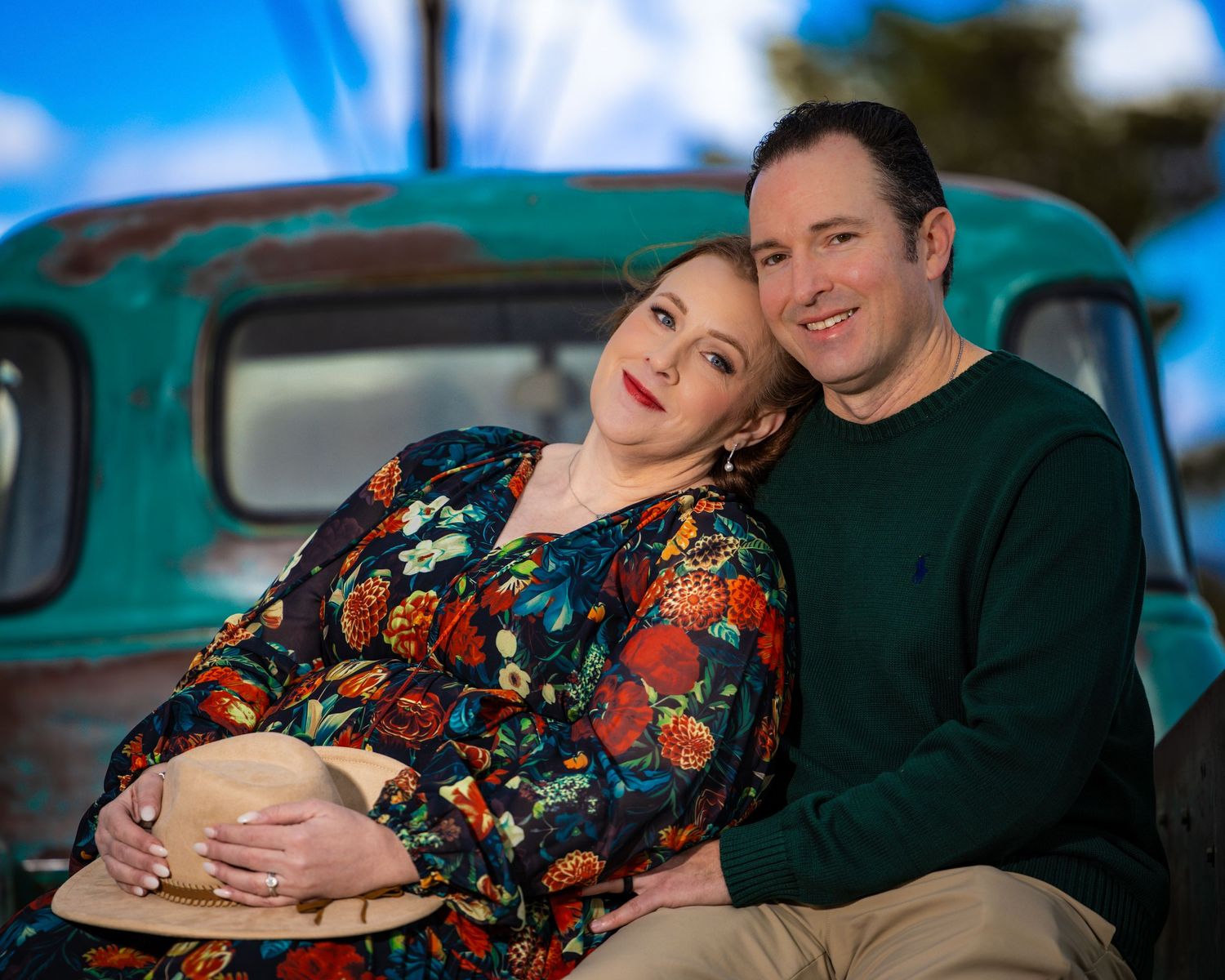 Couple poses together in front of vintage turquoise truck under blue skies.