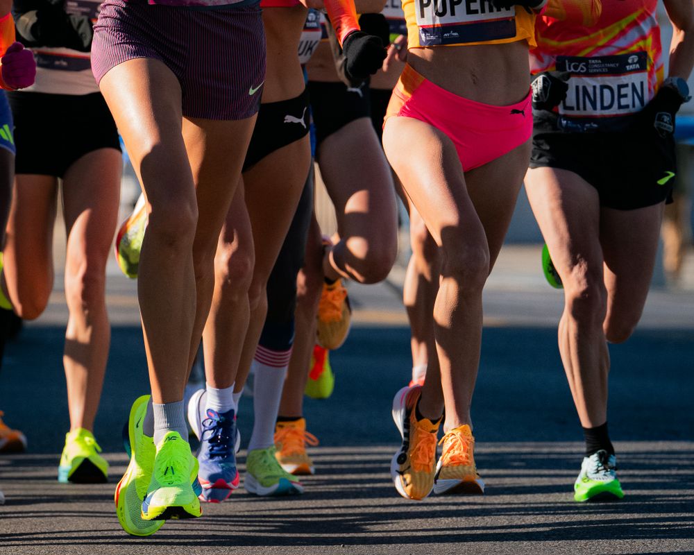 Multiple runners' legs and colorful running shoes in motion during a marathon race.