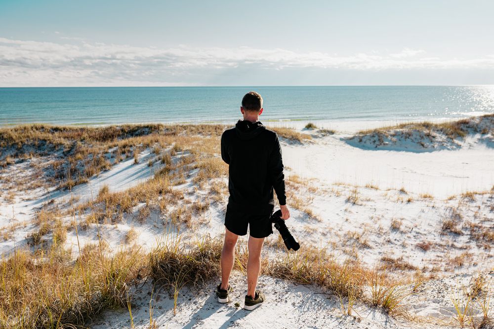 Figure walking on sandy path through snow-covered dunes with ocean view.