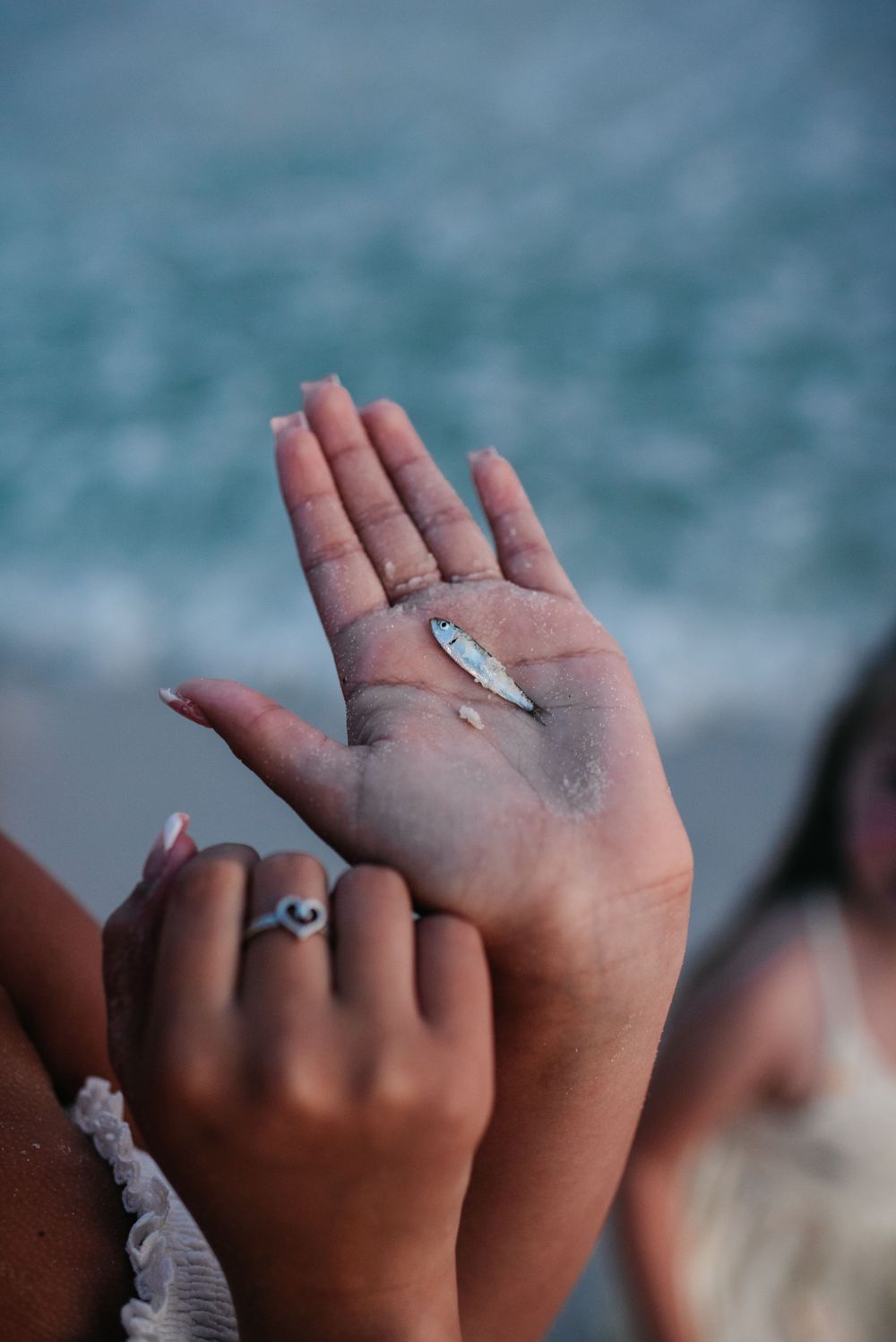 Close up of hands holding sand against blurred turquoise ocean backdrop.