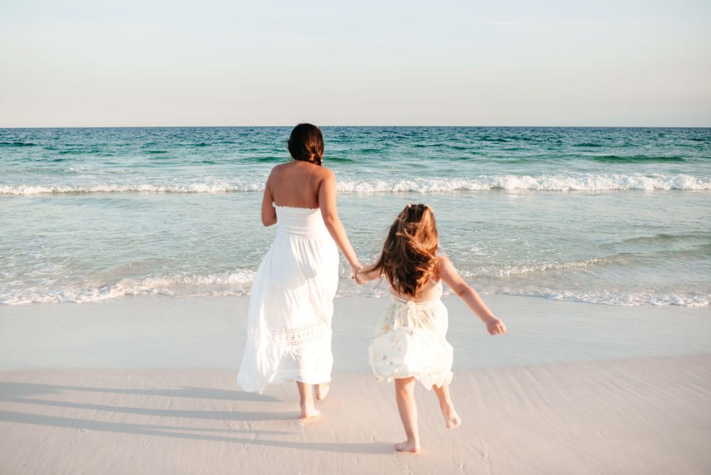 People walking and playing along a beautiful white sandy beach at sunset with turquoise ocean waves.
