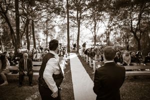 Black and white photo of wedding guests gathered outdoors under trees during ceremony.