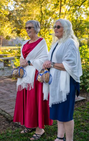 Women in red dresses and white shawls standing together outdoors at a wedding event.