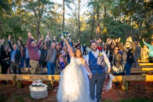 Wide shot of outdoor wedding ceremony with guests seated among trees at sunset.