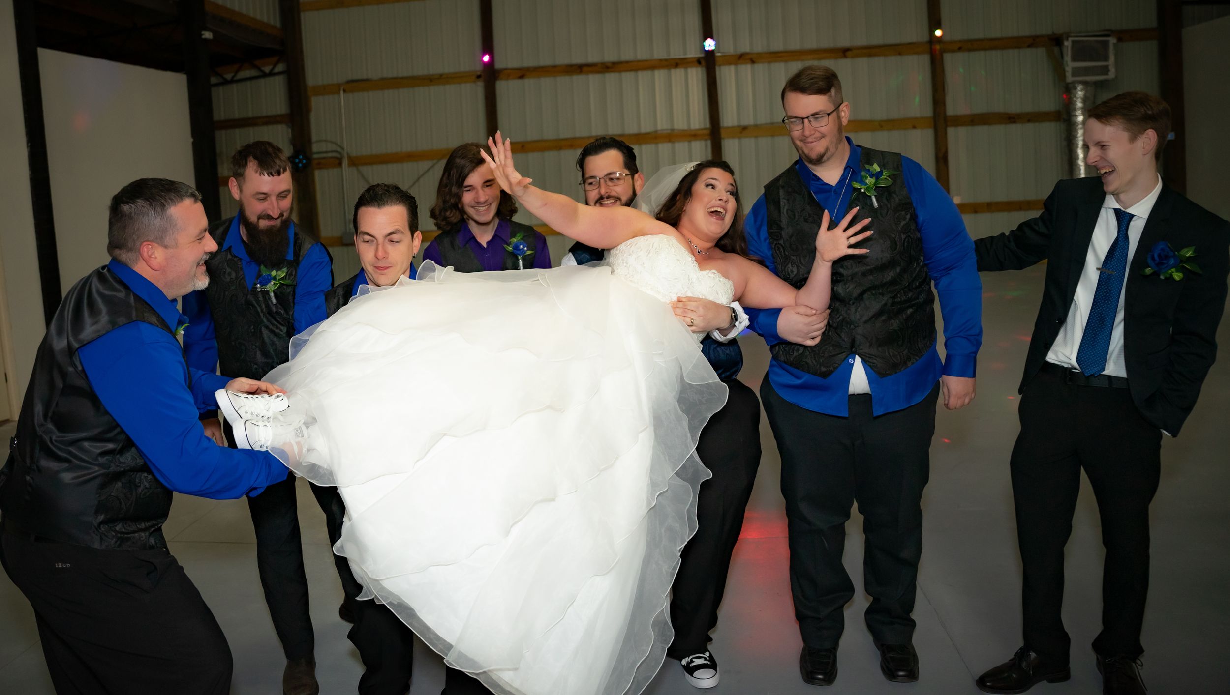 Wedding party lifts bride in white dress during reception celebration.