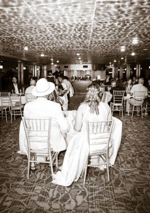 Black and white shot of reception venue with guests seated at tables under decorative ceiling.