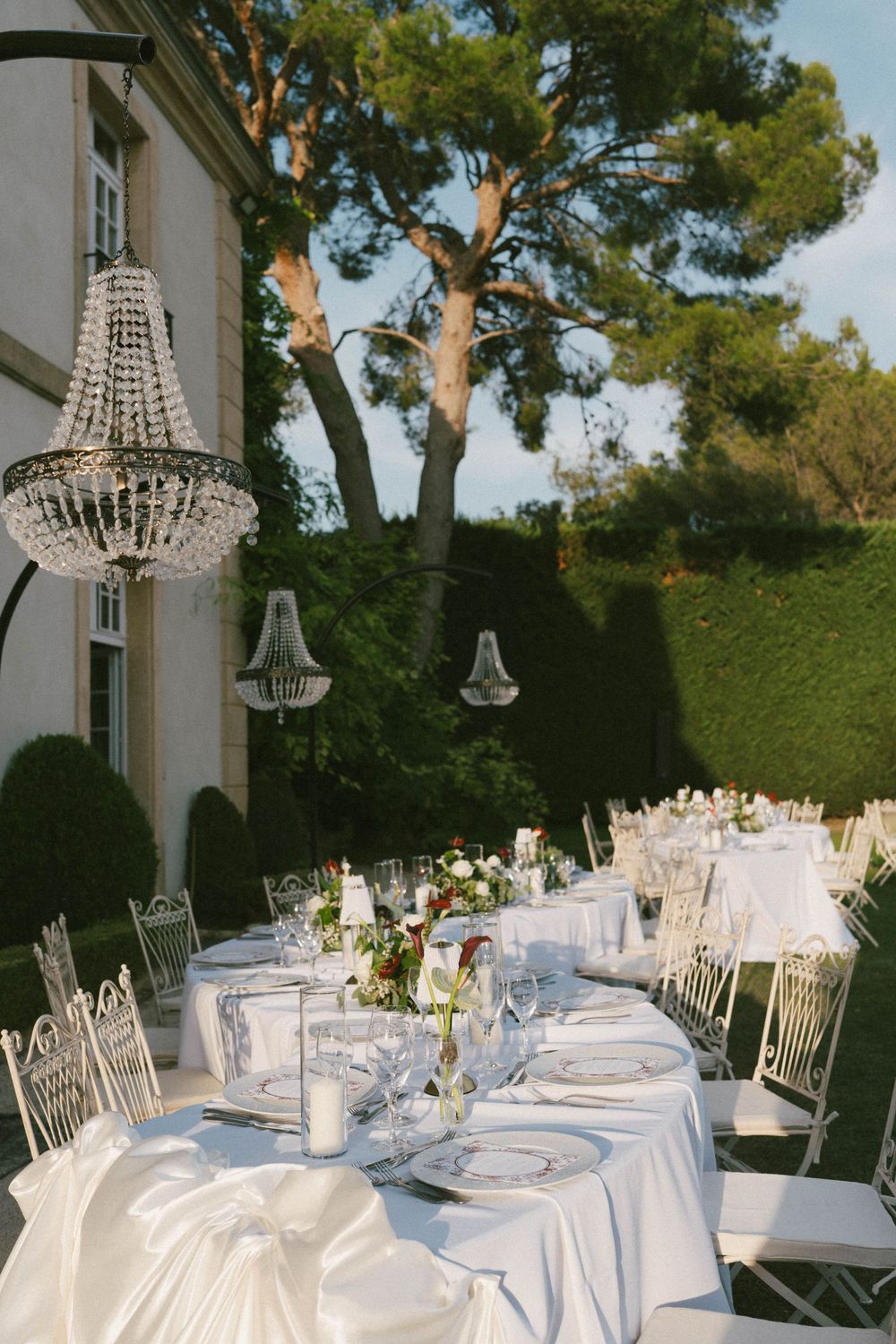 Elegant outdoor wedding reception with crystal chandeliers, white tablecloths, chiavari chairs, and floral centerpieces at a luxury villa.