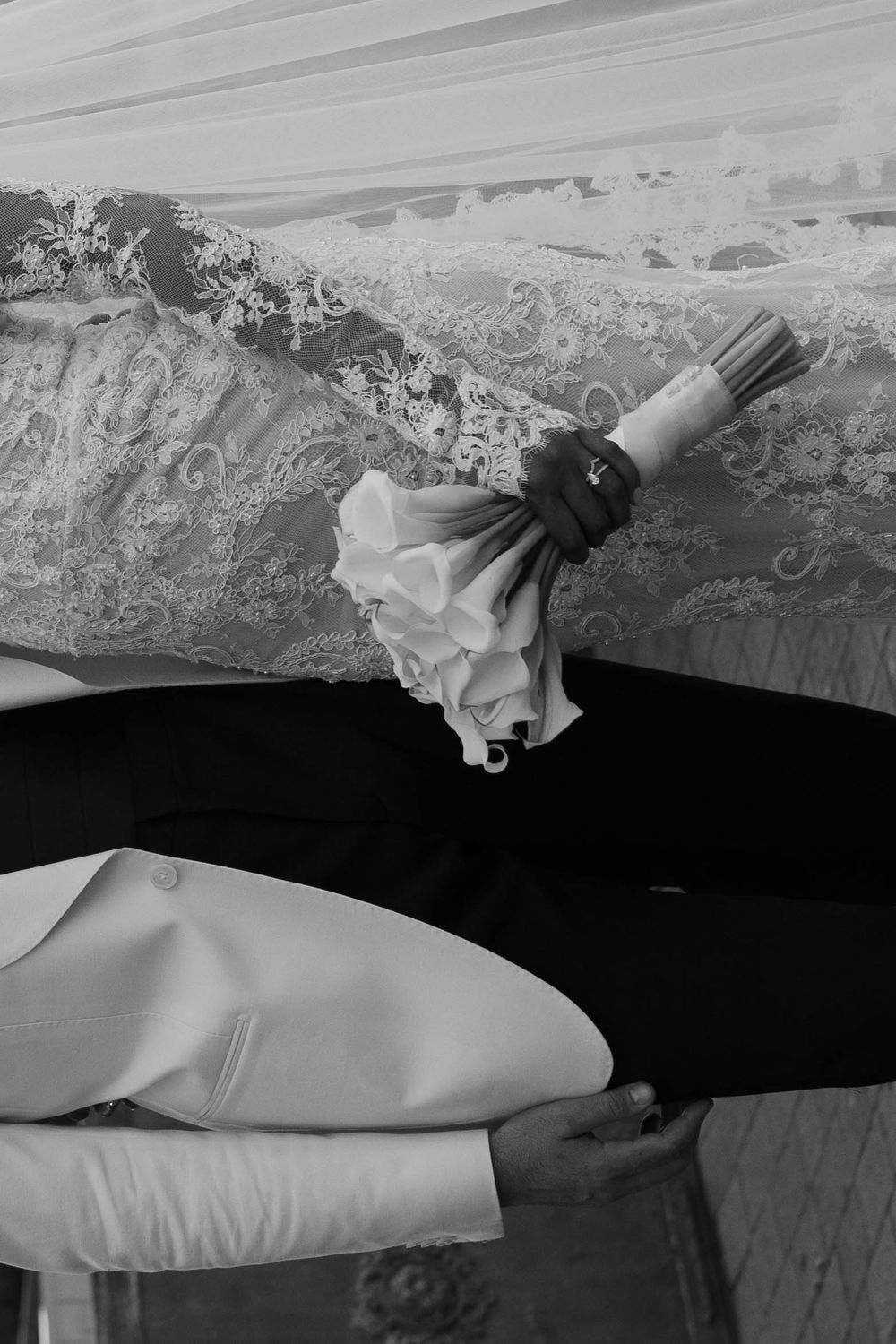 Black and white wedding photo of bride holding floral bouquet in lace dress beside groom in tuxedo.