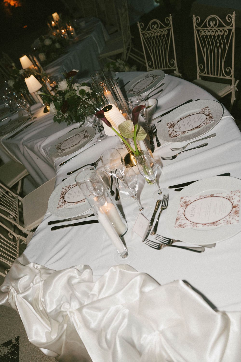 Elegant wedding reception table set with white linens, candles, floral centerpieces, and decorative menu cards.