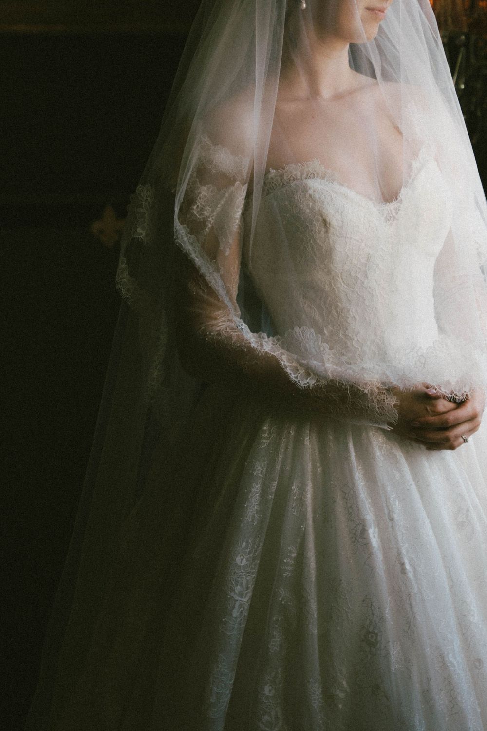 Portrait de mariée éthéré montrant les détails délicats en dentelle d'une robe de mariée à décolleté en cœur avec voile fluide.