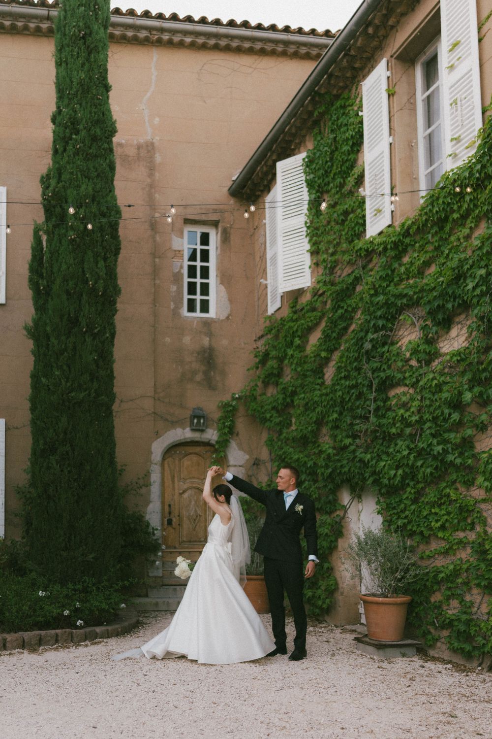 Bride and groom dancing outside a ivy-covered French chateau with cypress trees and string lights.