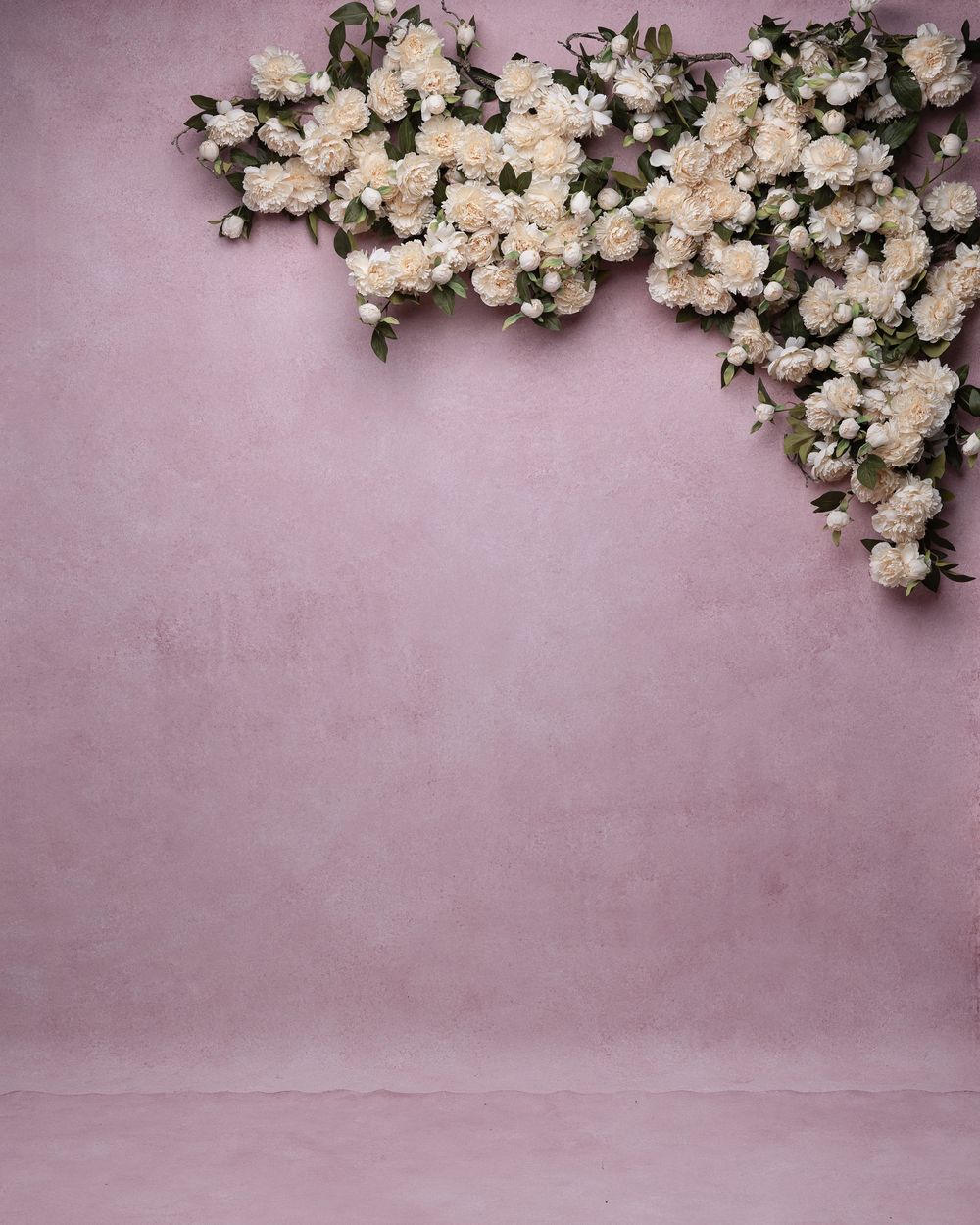 White floral branches with delicate blooms arranged against a soft mauve textured background in a minimalist composition.