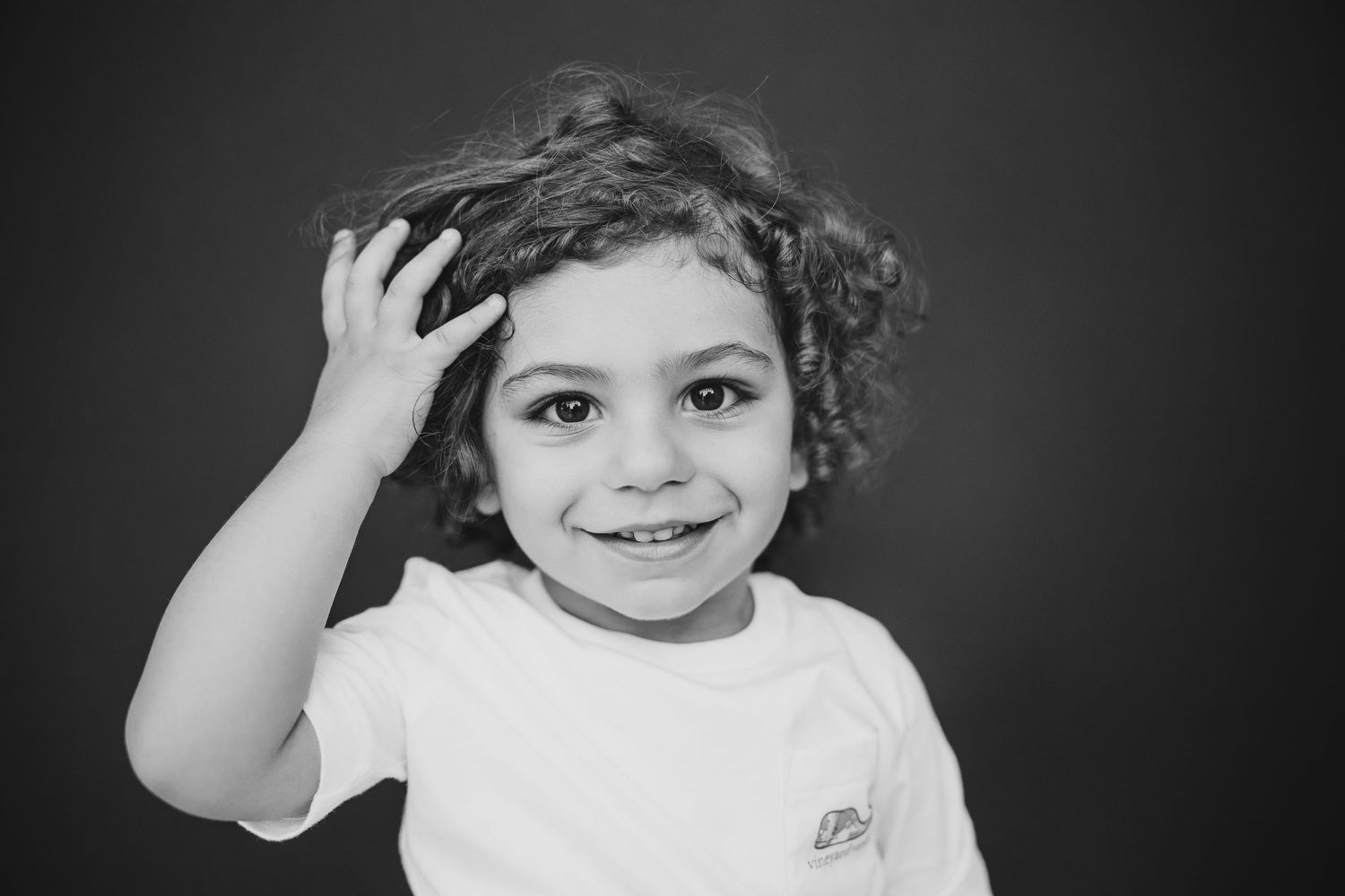 Portrait of a young child with curly hair wearing a gray henley shirt against a neutral background.