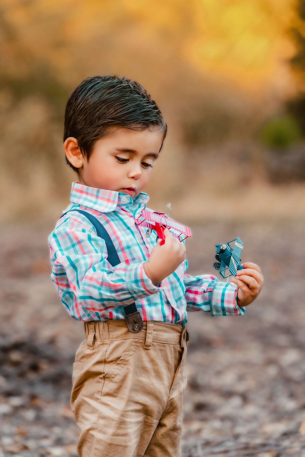 Child in plaid shirt and khakis playing with toys outdoors.