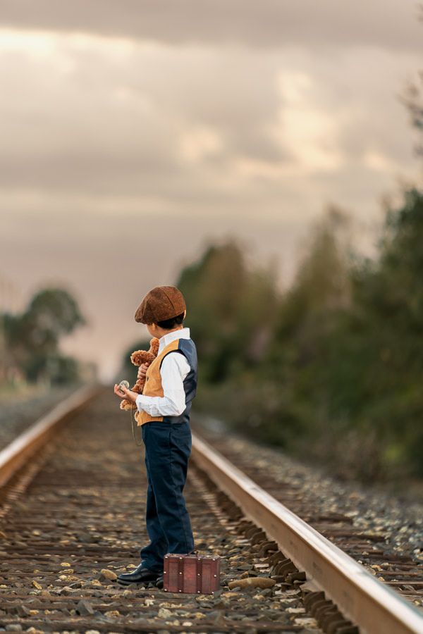 Small figure standing on train tracks with vintage suitcase at sunset.